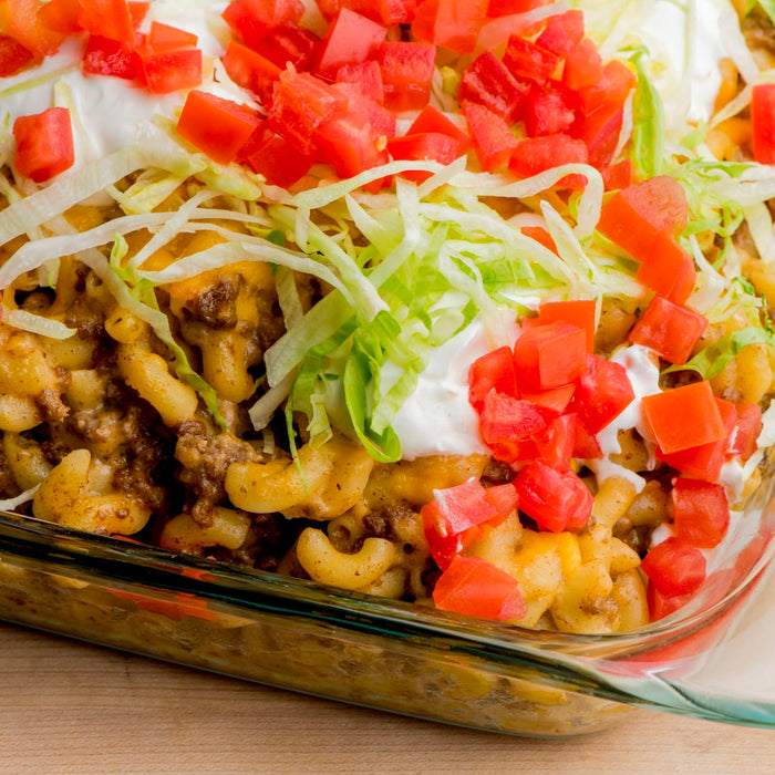 A close-up of a casserole dish filled with macaroni and cheese ground beef lettuce tomatoes and sour cream.