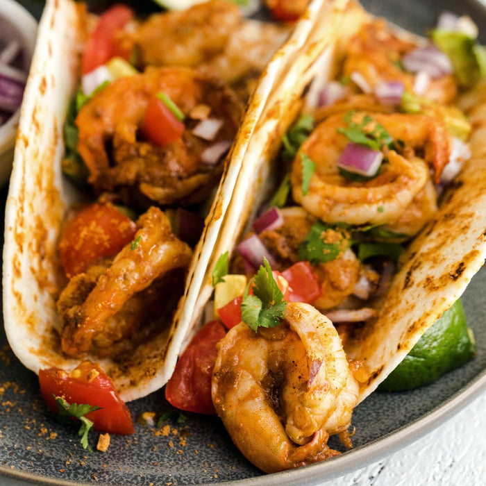 Two tacos filled with shrimp tomatoes onions and cilantro.