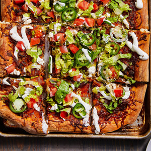 A close-up of a pizza with toppings of lettuce tomatoes jalapenos and sour cream.