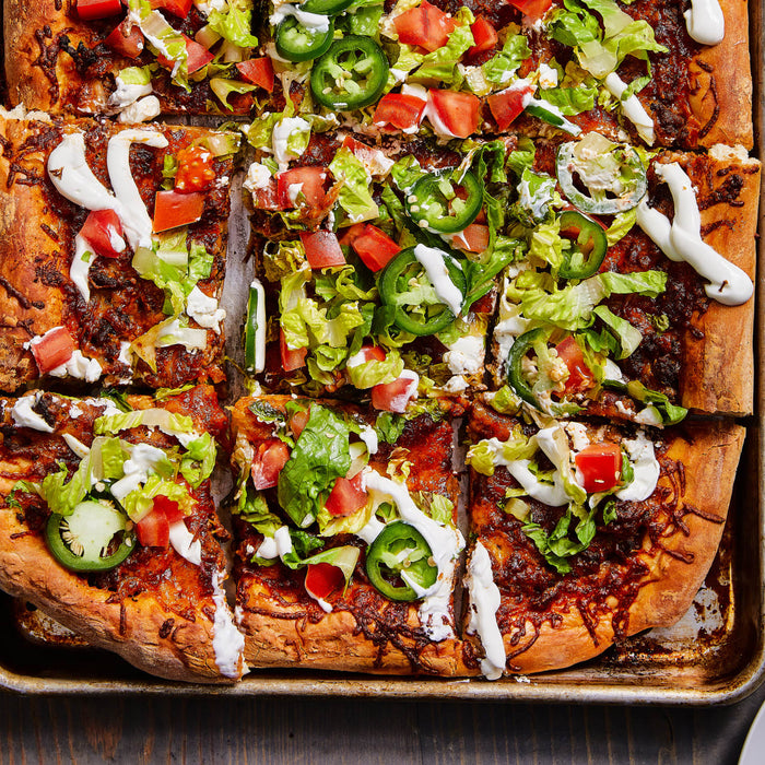 A close-up of a pizza with toppings of lettuce tomatoes jalapenos and sour cream.