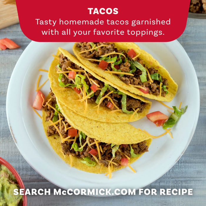 Three homemade hard-shell tacos, seasoned with Mccormick Organics Regular Taco Seasoning Mix 1 Oz, are presented on a white plate with toppings like lettuce, cheese, and tomatoes.