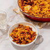 A hearty serving of cheesy beef and macaroni, a delicious recipe made with Mccormick Organics Regular Taco Seasoning Mix 1 Oz, is presented in a white bowl with the skillet in the background.
