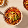 A hearty bowl of chicken fajita soup, made with Mccormick Organics Regular Fajita Seasoning Mix 1 Oz, is garnished with fresh avocado, tortilla strips, and a slice of jalapeño.
