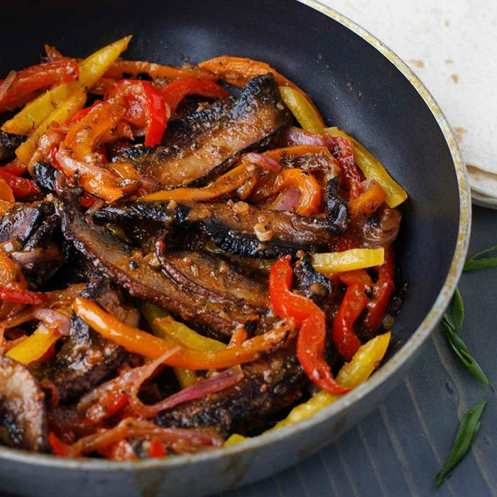 A skillet of delicious portobello mushroom fajitas made with Mccormick Organics Regular Fajita Seasoning Mix 1 Oz sits ready to be served with tortillas.