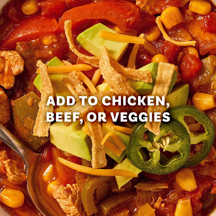 A close-up of a hearty bowl of tortilla soup, made with Mccormick Organics Regular Fajita Seasoning Mix 1 Oz, is topped with avocado, cheese, tortilla strips, and jalapeños, illustrating a delicious serving suggestion.