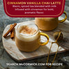 A warm cup of McCormick Cinnamon Vanilla Chai Latte is shown with cinnamon sticks and a tea strainer.