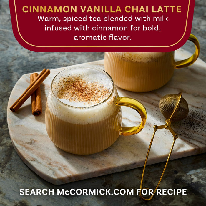 A warm cup of McCormick Cinnamon Vanilla Chai Latte is shown with cinnamon sticks and a tea strainer.