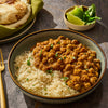 A bowl of chickpea curry served over rice, accompanied by naan bread and lime wedges.