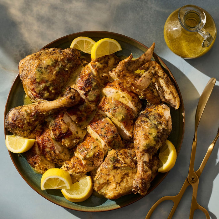 A plate of spatchcocked chicken with lemon wedges, ready to be served.