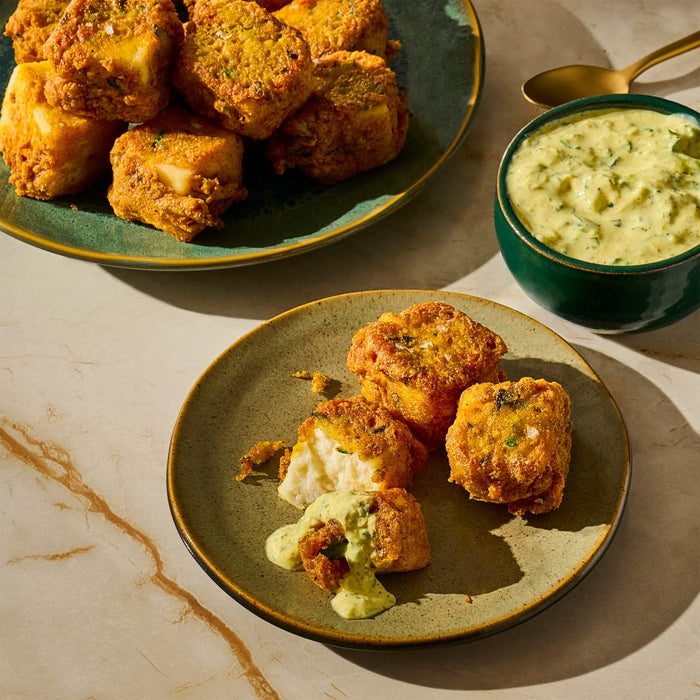 A plate of golden fried paneer cheese cubes is served with a creamy green dipping sauce.