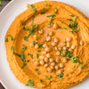 A close-up of a bowl of hummus topped with chickpeas and parsley.