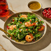 A vibrant shrimp salad with arugula, pomegranate seeds, and a light dressing is presented on a plate, showcasing a fresh and appetizing meal option.