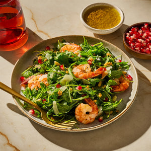 A vibrant shrimp salad with arugula, pomegranate seeds, and a light dressing is presented on a plate, showcasing a fresh and appetizing meal option.