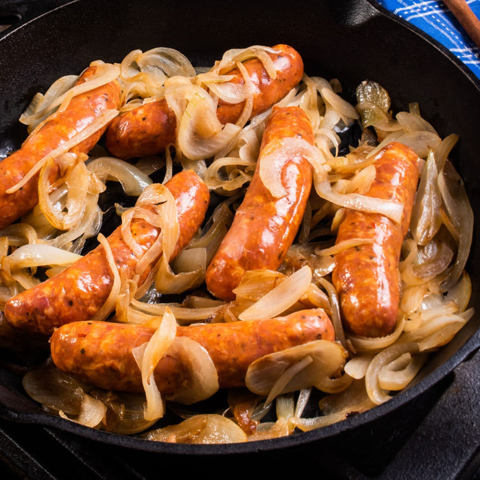 A close-up of a cast iron skillet filled with cooked sausage and onions.