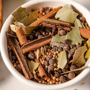 A white bowl filled with a variety of spices including cinnamon sticks bay leaves and peppercorns.