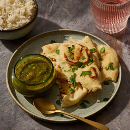 A plate of naan bread with a green dipping sauce, accompanied by rice and a drink, showcasing a delicious meal.