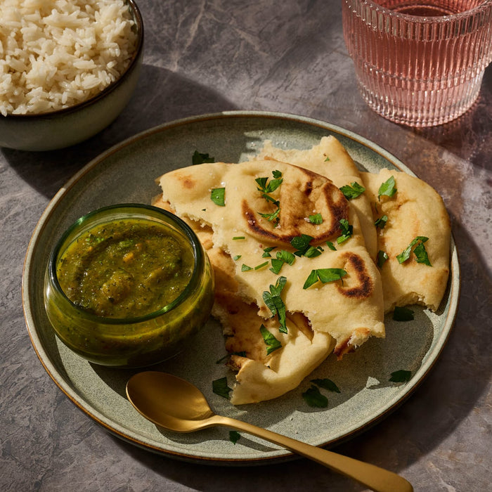 A plate of naan bread with a green dipping sauce, accompanied by rice and a drink, showcasing a delicious meal.