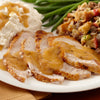 A white plate holds a traditional holiday meal featuring sliced turkey breast covered in savory gravy alongside mashed potatoes, green beans, and stuffing.