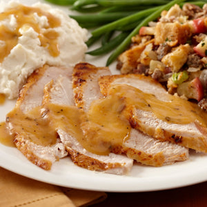 A white plate holds a traditional holiday meal featuring sliced turkey breast covered in savory gravy alongside mashed potatoes, green beans, and stuffing.