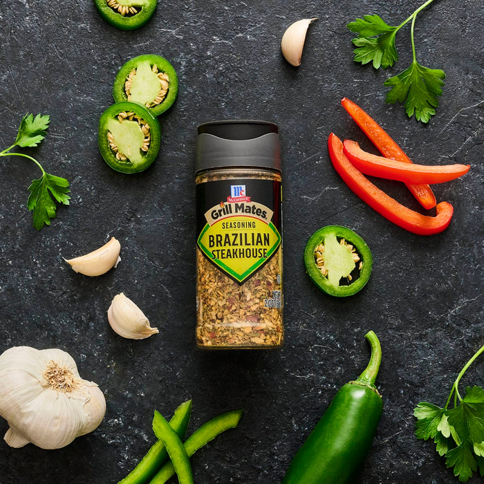 A bottle of Grill Mates Brazilian Steakhouse seasoning is surrounded by fresh ingredients like garlic, jalapenos, red peppers, and parsley.