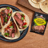 Three tacos filled with grilled steak and salsa are displayed next to a packet of McCormick Grill Mates Brazilian Steakhouse seasoning.
