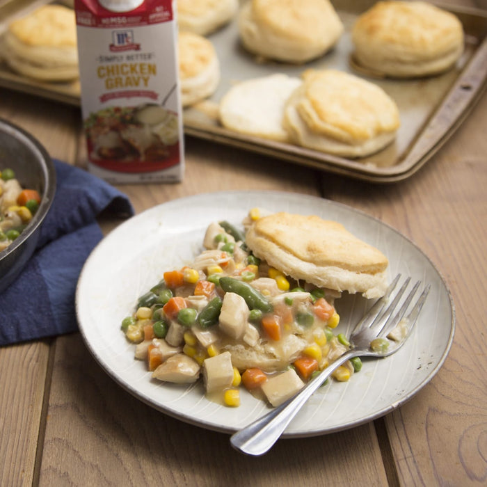 A plate of chicken pot pie with a biscuit and a fork with a carton of McCormick Simply Better Chicken Gravy in the background.