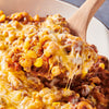 A wooden spoon scoops up a cheesy, meaty pasta dish.