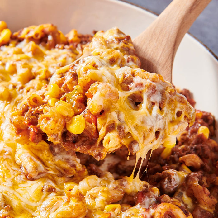 A wooden spoon scoops up a cheesy, meaty pasta dish.