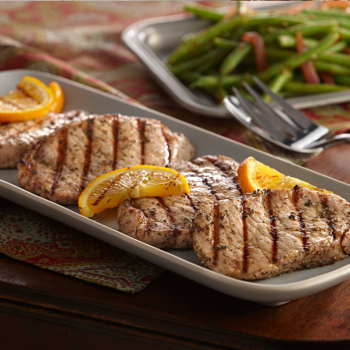 A plate of grilled pork chops garnished with orange slices, served with a side of green beans.