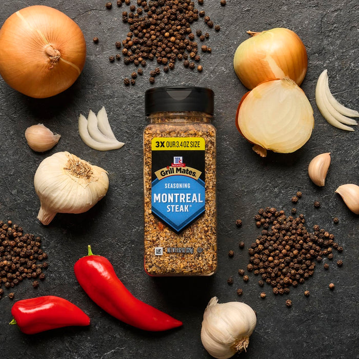 The image showcases McCormick Montreal Steak Seasoning surrounded by fresh ingredients like garlic, onion, red pepper, and spices, highlighting the seasoning's composition and flavor profile.
