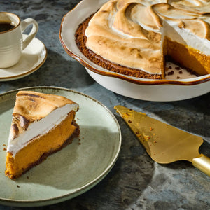 A slice of sweet potato pie with toasted meringue topping sits on a plate next to the whole pie and a cup of coffee.