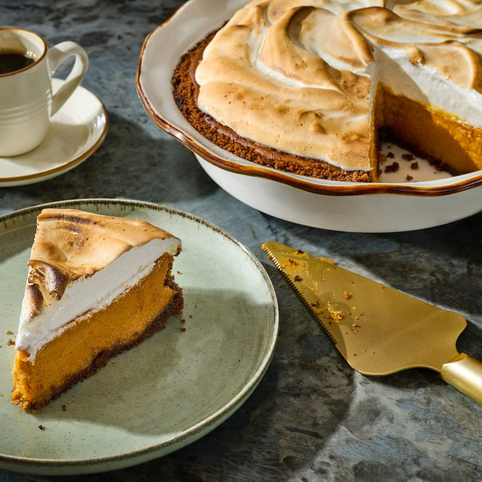 A slice of sweet potato pie with toasted meringue topping sits on a plate next to the whole pie and a cup of coffee.