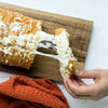 A hand pulls a cheesy slice of pull-apart bread seasoned with Mccormick Garlic And Herb Pepper Seasoning Ground 4.37 Oz from a loaf on a wooden board.