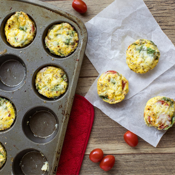Freshly baked egg muffins seasoned with Mccormick Garlic And Herb Pepper Seasoning Ground 4.37 Oz are displayed in a muffin tin and on parchment paper alongside cherry tomatoes.