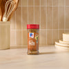 A bottle of Mccormick Signature Seasoning Savory Garlic Onion Oz stands on a marble countertop in a bright kitchen setting with cooking utensils and stacked plates in the background.