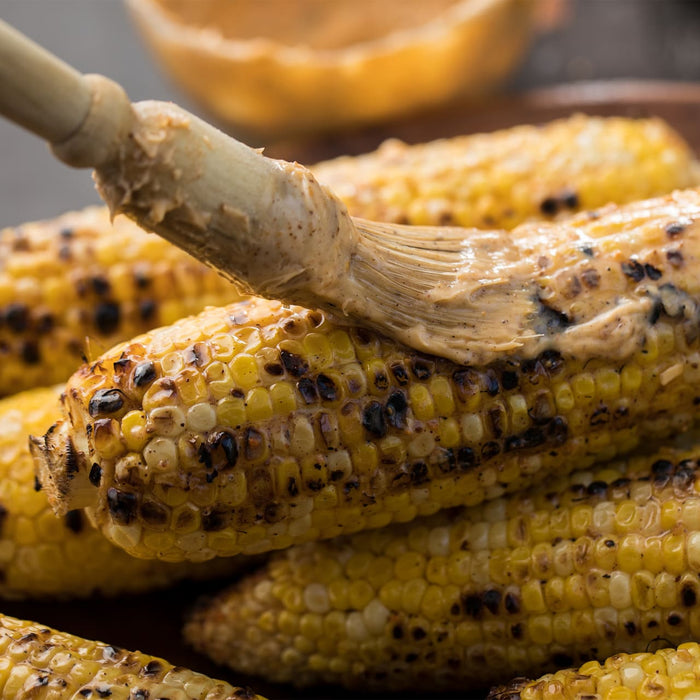 Grilled corn on the cob being brushed with a flavorful sauce.