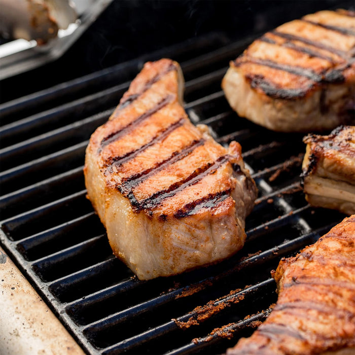 Grilled pork chops with distinct grill marks are cooking on a barbecue grill.