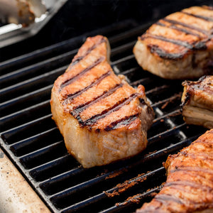 Grilled pork chops with distinct grill marks are cooking on a barbecue grill.