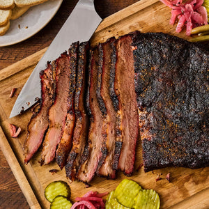 A perfectly smoked brisket sliced on a wooden board is seasoned with Mccormick Grill Mates Mesquite Seasoning Rub 4.87 Oz and served with pickles and onions.