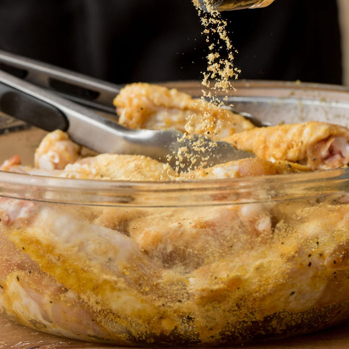 Chicken wings are being seasoned in a glass bowl with tongs nearby, ready for cooking.