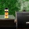 A bottle of Traeger Rub sits on a grill, suggesting outdoor cooking and flavor enhancement.