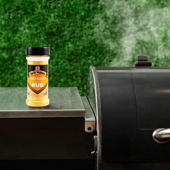 A bottle of Traeger Rub sits on a grill, suggesting outdoor cooking and flavor enhancement.