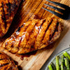 Grilled chicken breast with grill marks on a wooden board, served with asparagus.