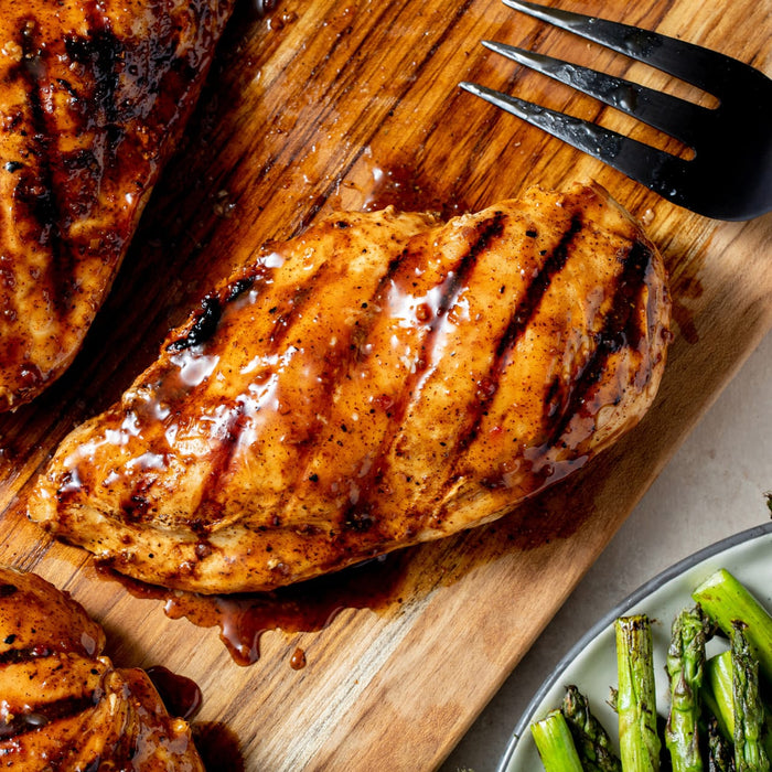 Grilled chicken breast with grill marks on a wooden board, served with asparagus.