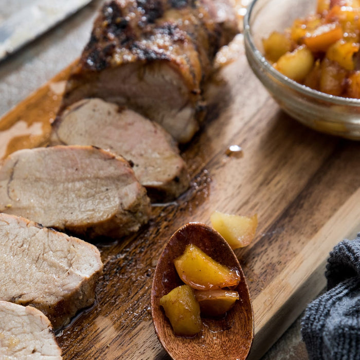 A sliced pork tenderloin is presented on a wooden board with a side of apple chutney, suggesting a delicious and balanced meal.