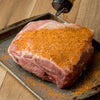 A pork shoulder roast is being seasoned with a spice rub on a baking sheet.