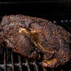 A smoked pork shoulder with a dark, flavorful crust sits on a grill.