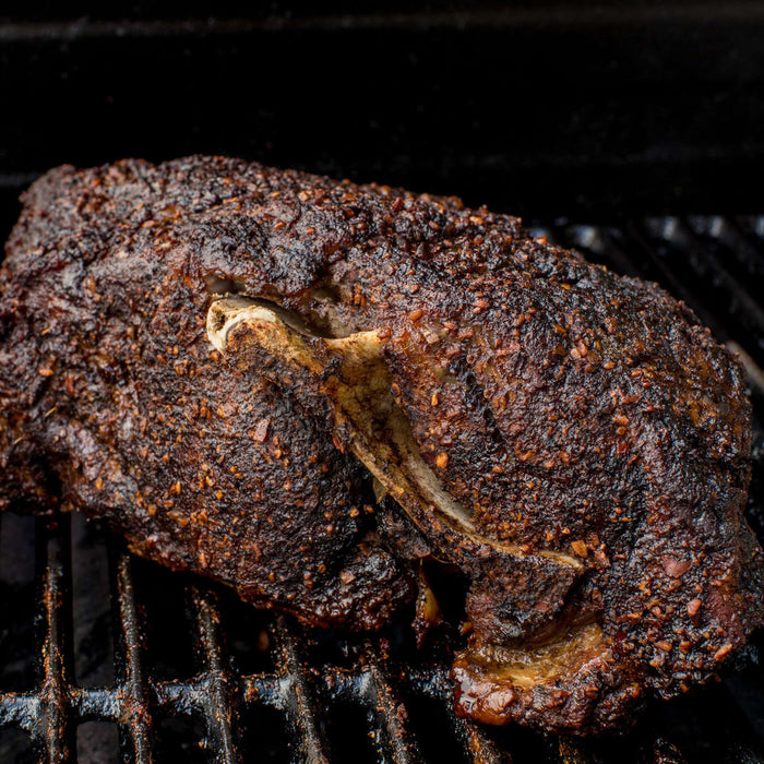 A smoked pork shoulder with a dark, flavorful crust sits on a grill.