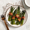 A white plate holds five bundles of roasted asparagus wrapped in crispy bacon and seasoned with Mccormick Himalayan Pink Salt Pepper And Garlic Seasoning Ground 6.5 Oz.