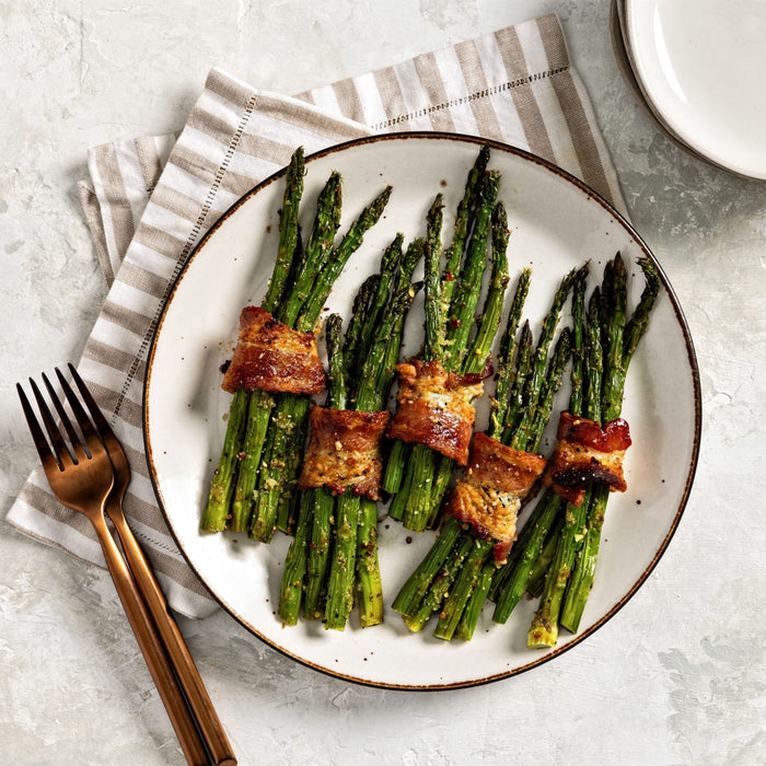 A white plate holds five bundles of roasted asparagus wrapped in crispy bacon and seasoned with Mccormick Himalayan Pink Salt Pepper And Garlic Seasoning Ground 6.5 Oz.